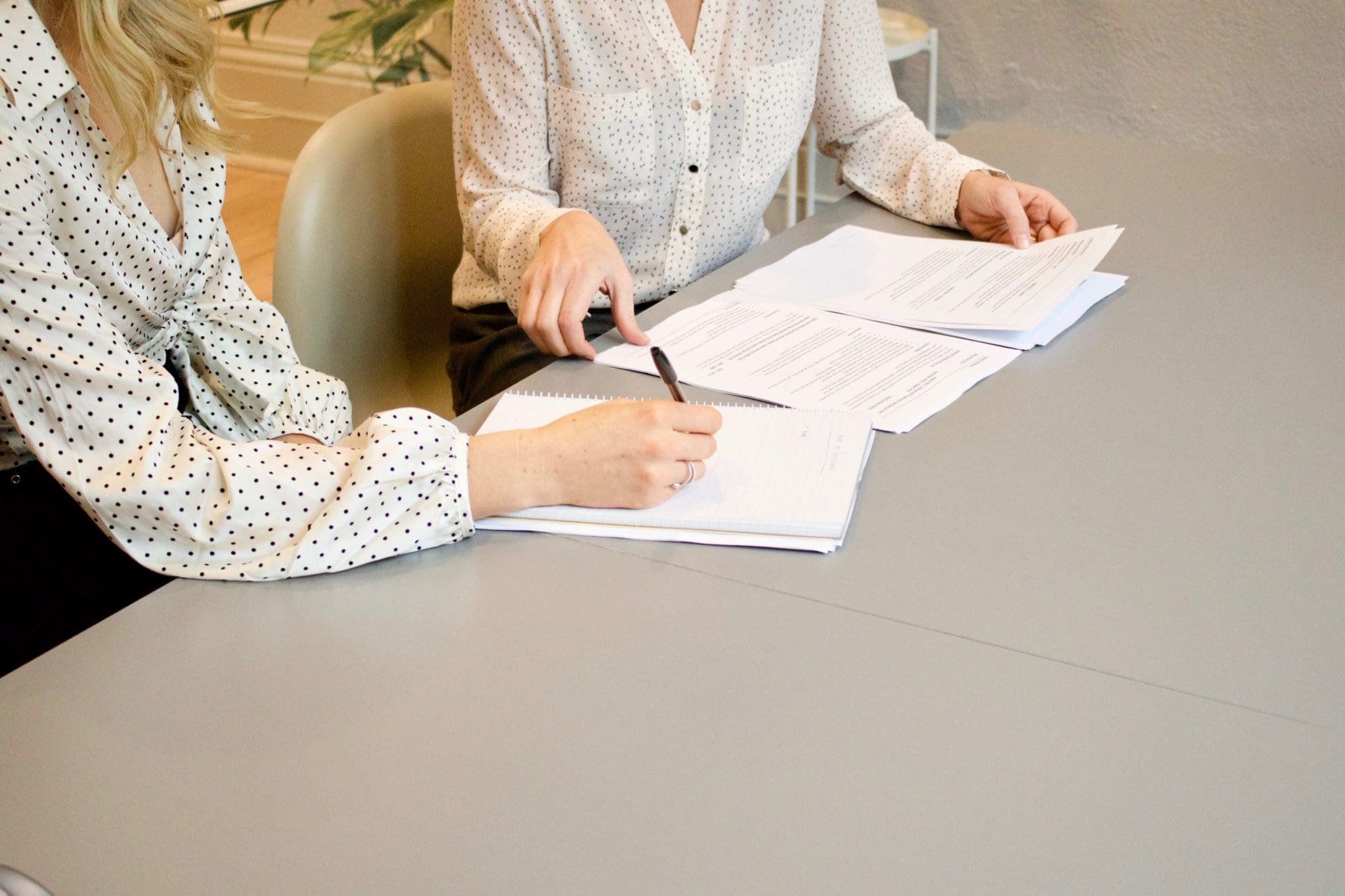 two woman at desk exchange paperwork